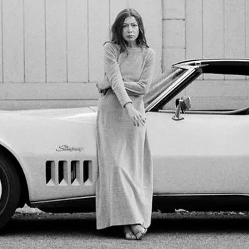 Joan Didion standing leaning on a car